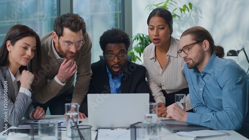 Multiracial business team partners managers looking in laptop with shock amazed wonder reading good online news work success at office meeting. Multiethnic five workers surprised with computer achieve