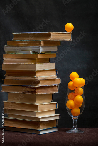 Still life with a stack of books and orange balls in a glass.