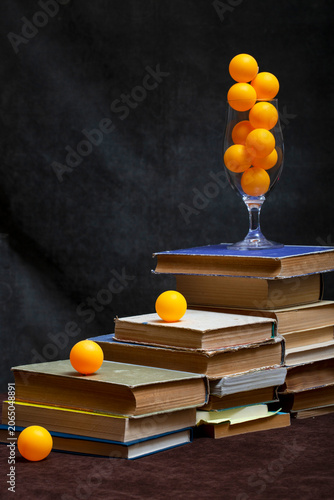 Still life with a stack of books and orange balls in a glass.