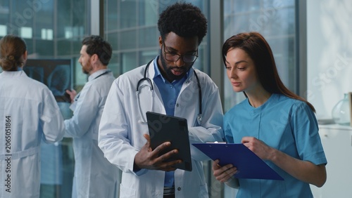 Two diversity doctors man with woman discussing medical examination using digital tablet together in hospital. Caucasian female therapist doctor talking with African American male surgeon at clinic