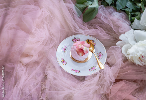 Foto Elegant pink dessert served on a vintage floral plate with a golden spoon, surrounded by soft tulle fabric and peony blossoms