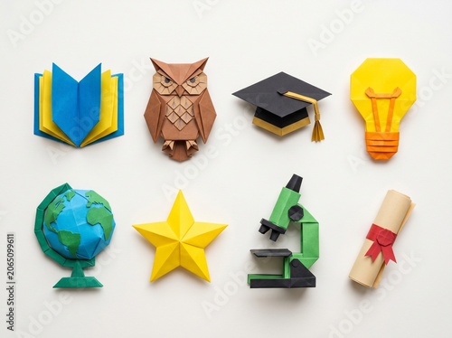 Beautiful origami paper craft set of educational symbols. Flat lay of folded paper school book, owl, graduation cap, microscope, and globe.
