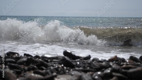 A view of large waves moving slowly. Muddy waves rise and crash against the rocky shore, forming foam. The sea during a storm.
