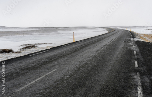 Winding black asphalt road extending through an empty snowy icelandic winter landscape, offering a sense of travel and solitude