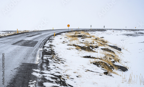 Snowy frozen Asphalt road curving through a vast, snow covered winter landscape in iceland, emphasizing solitude and travel
