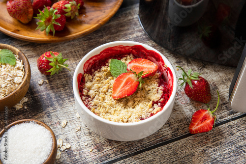Healthy cooking with air fryer: homemade dessert traditional English crumble cake with strawberry on a wooden table.