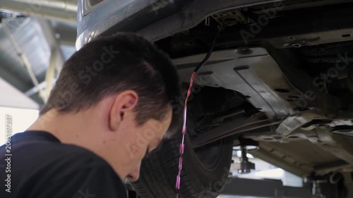 Auto repair - pink antifreeze is flowing out of the hose. The mechanic is draining the antifreeze from the hose underneath the bottom of the car. The car is being serviced at a car service station.