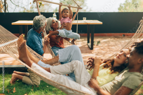 Multi-generational diverse family relaxing playing together in garden hammock