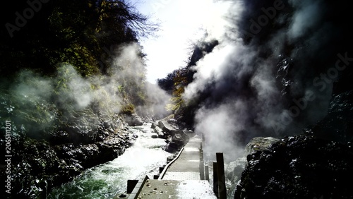 Foto Thick steam plumes billow from rugged canyon walls over a flowing river and a na