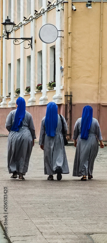 Three nuns in gray robes and blue headscarves are walking