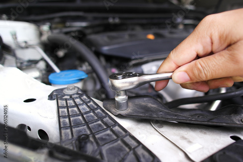 Obraz na plátne Hand using a socket ratchet wrench to tighten or loosen a bolt under a car hood