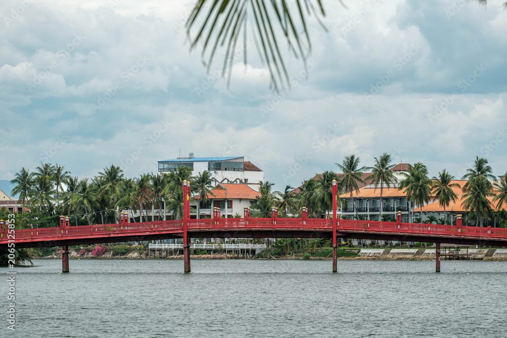 Obraz premium Red wooden pedestrian footbridge over a wide river in a tropical country