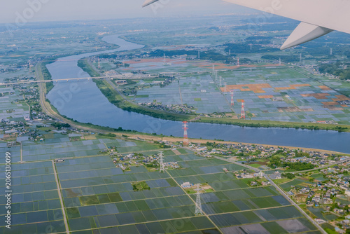 Aerial view from an airplane window during final approach to Narita Airport, capturing Chiba rural landscape with green rice fields, winding rivers, and a distant horse training track, Japan.