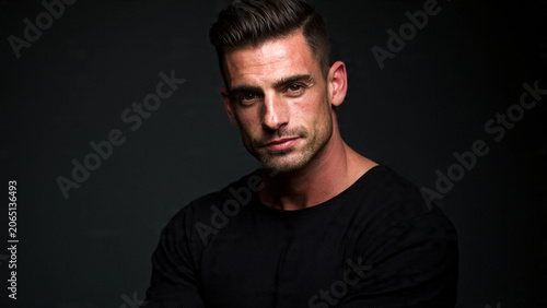Confident man in black shirt posing against dark background