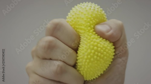 Hand squeezing a textured yellow stress ball in a neutral background, showcasing the gradual compression and deformation of the object in three sequential frames