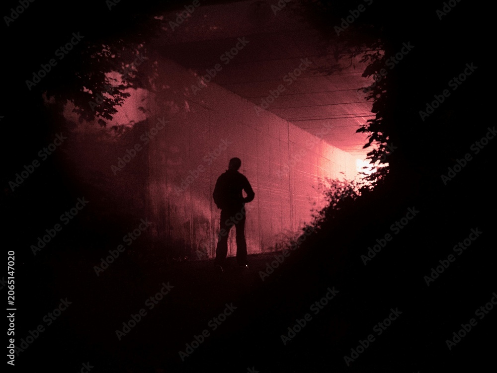 Fototapeta premium Dramatic silhouette of lonely man in dark tunnel under red light evoking mystery, danger, and suspense for cinematic thriller posters.
