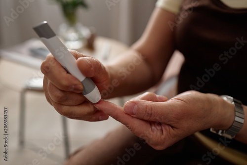 Close up of woman pricking fingertip with glucose meter lancet, monitoring blood sugar for diabetes management. Ideal for healthcare, chronic condition, wellness campaign use