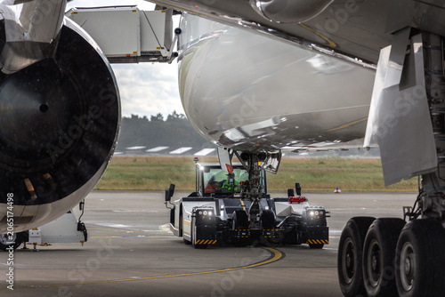 Foto Modern widebody big long haul jet aircraft towed by ground vehicle on airport taxiway tarmac rainy weather