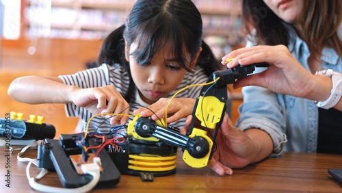 Canvastavla Cute Asian girl child building STEM robotic car project inside modern school library space with female mentor
