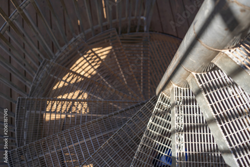 Industrial metal spiral stairs with deep shadows. Top down view of steel spiral staircase. High contrast metal staircase architecture