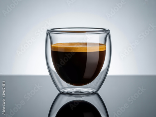 Double Walled Glass Cup Filled With Freshly Brewed Hot Espresso Coffee on a Reflective Surface