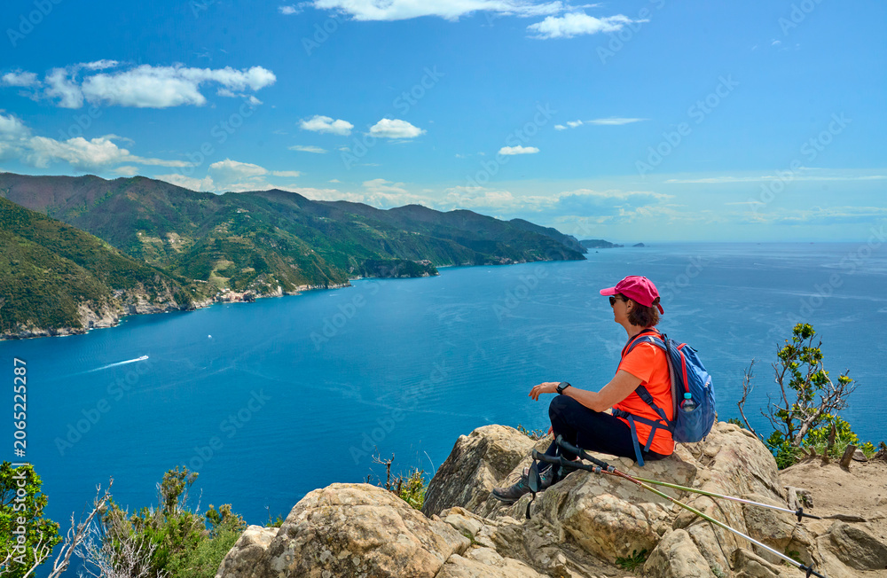 Obraz premium Active senior woman hiking hike above Monterosso ,Cinque Terre, Panoramic view of the Mediterranean Sea, dramatic coastline, lush hills, and picturesque village , Cinque Terre, Liguria, Italy. 