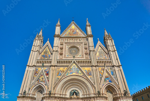  Orvieto Cathedral in Umbria, Italy, showcasing its ornate Gothic facade, colorful mosaics, rose window, and detailed stone carvings under a clear blue sky.