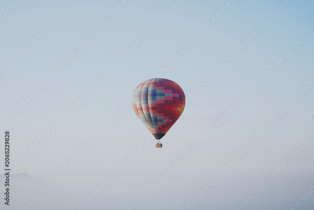 Fototapeta premium Colorful hot air balloon floating above the morning mist with a pastel blue sky