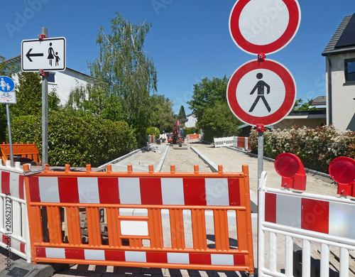 Road blocked and closed for work with red and white barrage, warning lights and stop signal, in view an excavator with shovel in pause