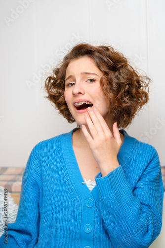 young woman with dental braces experiencing a toothache or oral discomfort, touching her jaw with a pained expression, highlighting orthodontic challenges and dental sensitivity