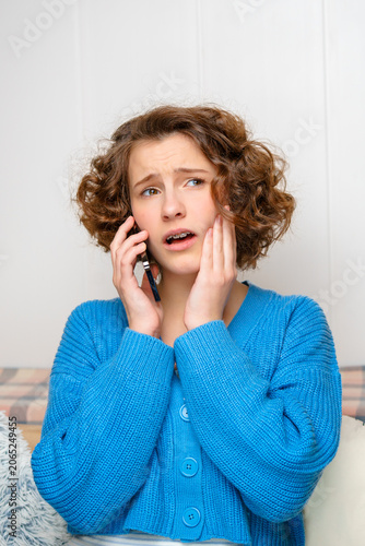 worried teenage girl with braces making a phone call, expressing concern and holding her jaw, possibly experiencing toothache or dental discomfort