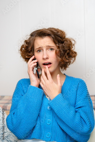 distressed young woman with curly hair on a phone call, reacting to shocking news with a worried expression, touching her mouth in disbelief.