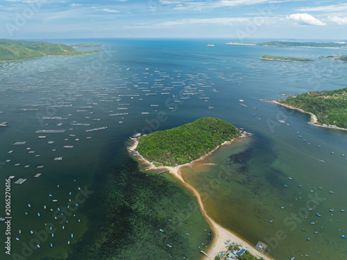 Drone panorama of a small green island surrounded by aquaculture farms in coastal waters near Song Cau town, Dak Lak province.