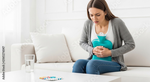 Woman with hot water bottle on stomach, experiencing pain, symbolizing discomfort, illness, and relief, representing healthcare or home remedies