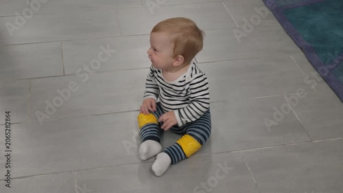 Happy child explores surroundings. Toddler cautiously inches forward. Infant demonstrating curiosity on living room floor. Baby moving unsteadily across tiled area in striped attire
