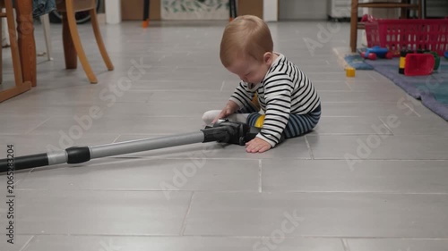 Infant investigates household items eagerly. Young child examines vacuum nozzle with curiosity and delight. Baby eagerly explores domestic setting and household objects with curiosity and joy