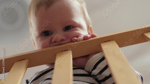 Curious child explores surroundings. Innocent toddler joyfully surveys nearby environment. Cheerful baby peeks curiously over wooden railing