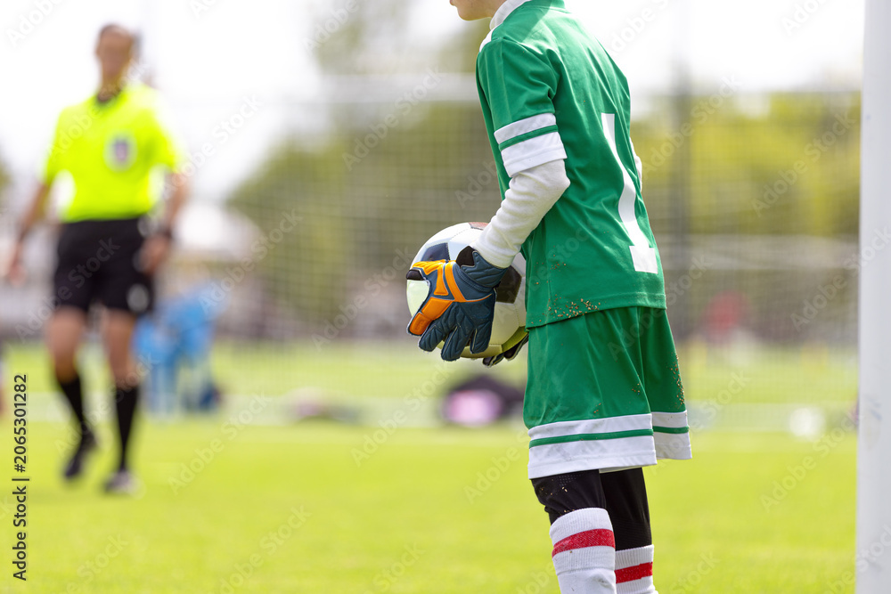 Naklejka premium Young Goalkeeper Holding Ball: Youth Soccer Player in Green Uniform Preparing for Goal Kick