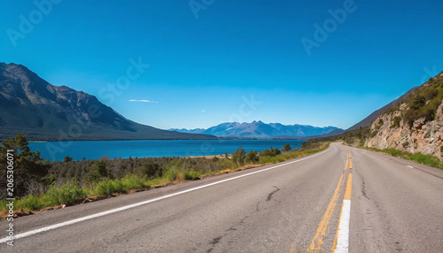 Asphalt road and blue lake with mountain nature landscape under blue sky.