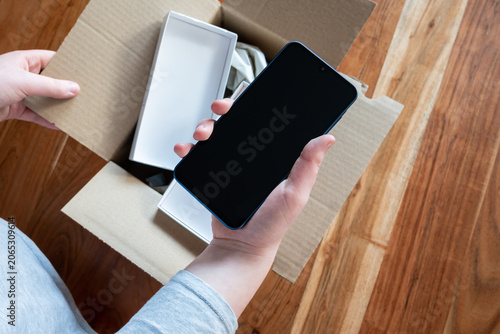 Hand holding new mobile phone after delivery. Unpacking the box with smartphone.