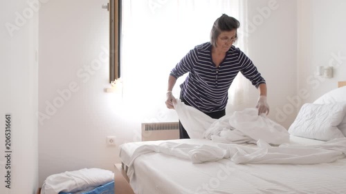 Senior woman removing used bed sheets while preparing a clean guest room