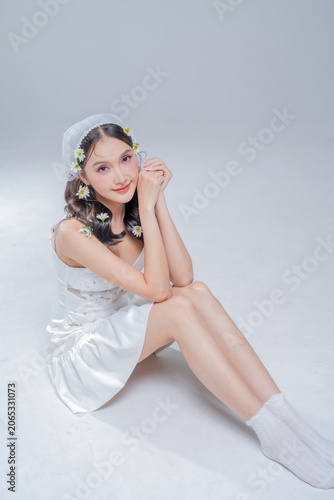 Obraz na plátne Elegant young Asian woman crouching in white satin dress with daisy flowers in h