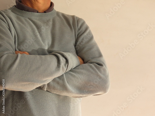 Closeup of a man in a sweater with crossed arms on a bright white background.