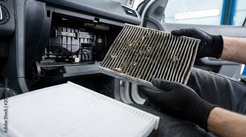 Dirty automotive air filter held by mechanic wearing gloves inside a vehicle dashboard cabin dust