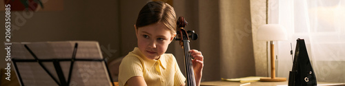 Canvas Print Child girl studying music and playing cello while reading sheet notes at home, expressing arts education and skill development