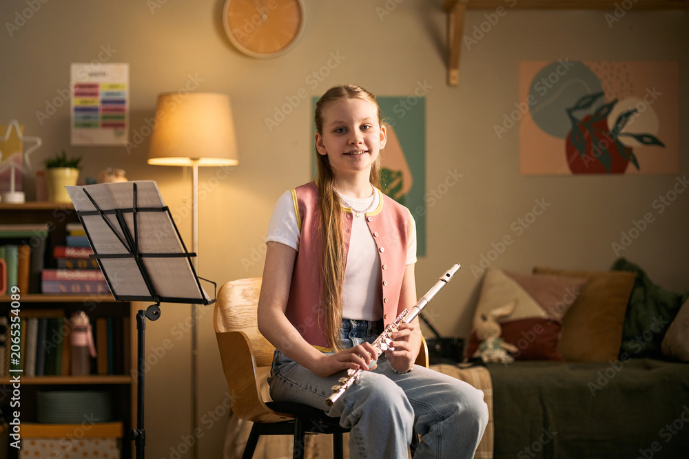 © DragonImages - Portrait of Caucasian girl studying music and holding flute during home practice, representing arts education and skill development. Useful for music lessons, tutoring, youth learning