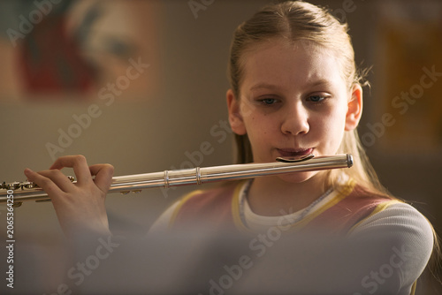 Obraz na płótnie Caucasian girl playing flute during music lesson, practicing instrument skills and arts education