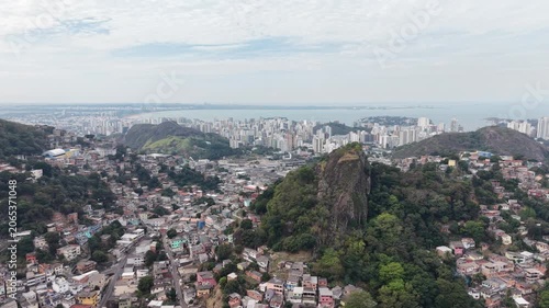 Panoramic aerial view of Vitória, Espírito Santo, Brazil, showcasing the urban skyline, bays, islands, hills, and coastal landscape beneath a dramatic cloudy sky.