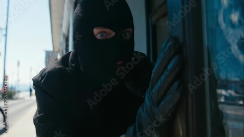 Criminal hides at entrance with alarmed eyes. He peers outside carefully as emergency situation unfolds on street