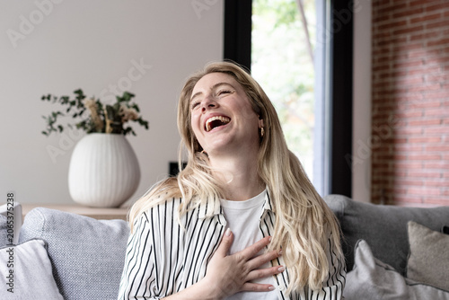 Φωτογραφία Happy young adult woman laughing out loud with her hand on her chest, sitting re